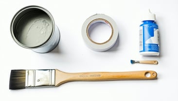 Flat lay of various decorating products on a clean white background Include a metal paint can undented a paintbrush a roll of masking tape a caulking nozzle and a small tub of filler All items should appear new and unblemished arranged clearly and fu-1